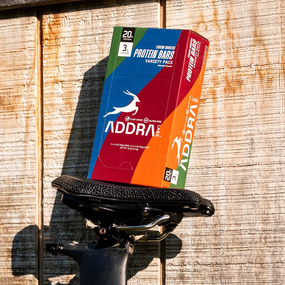 ADDRA 8 Count Starter Box resting on a bike saddle, showing 20g protein and 3g leucine on the pack