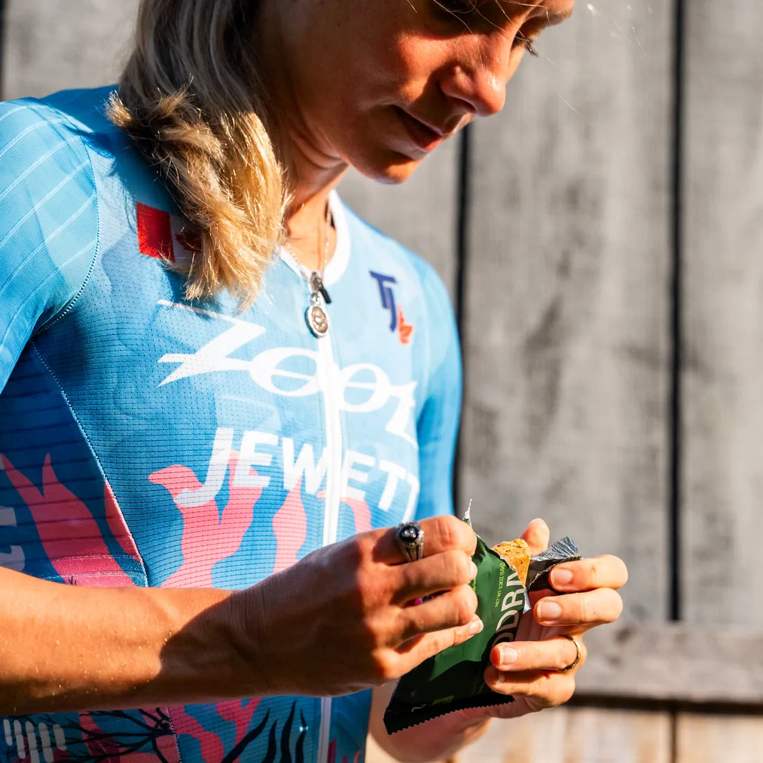 Triathlete in a Zoot race suit opening an ADDRA bar after a session, showing the soft baked texture inside