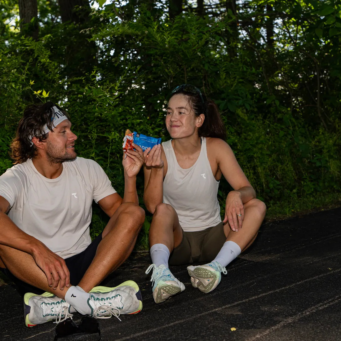 Two runners sitting on a road after a session, sharing ADDRA bars